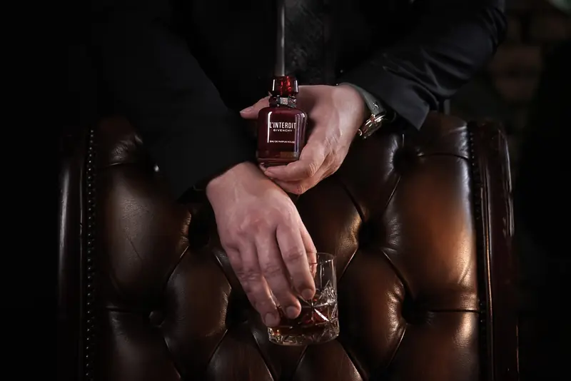 Givenchy L’Interdit Rouge parfüm egy kézben, sötét bőrfotel előtt